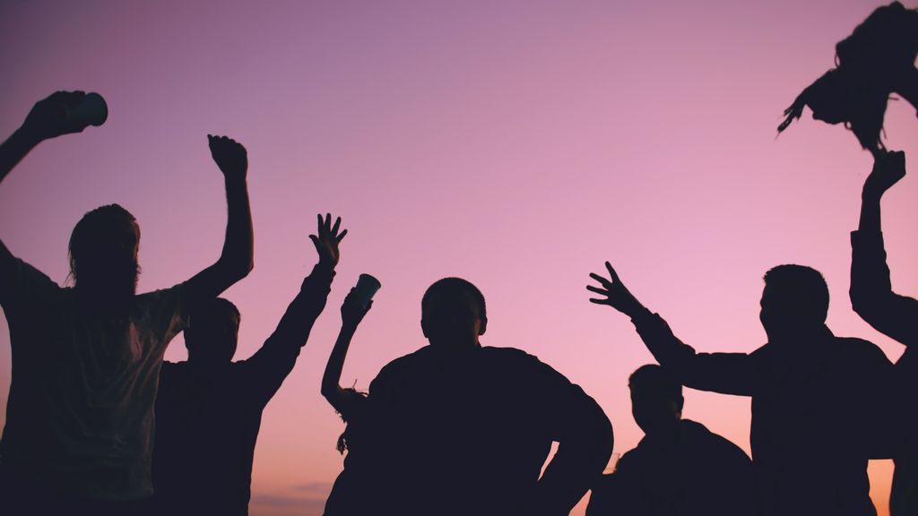 People celebrating outdoors with raised hands under a vibrant sunset sky.
